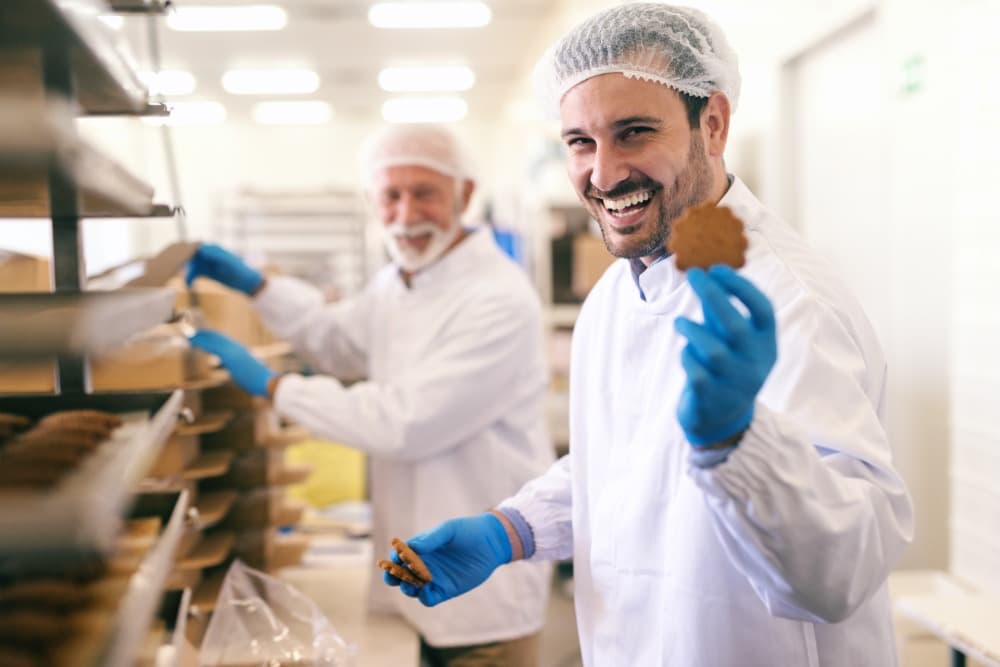Control de calidad en la industria de alimentos: Todo lo que necesitas saber para garantizar productos seguros 2 young smiling caucasian worker showing cookie while standing food factory 1